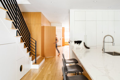 Mid-sized minimalist galley medium tone wood floor eat-in kitchen photo in New York with an undermount sink, flat-panel cabinets, white cabinets, marble countertops, white backsplash, subway tile backsplash, paneled appliances, an island and white countertops