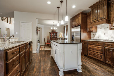 Inspiration for a mid-sized country u-shaped eat-in kitchen in Dallas with an undermount sink, raised-panel cabinets, dark wood cabinets, granite benchtops, white splashback, ceramic splashback, stainless steel appliances, dark hardwood floors, with island and brown floor.