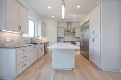 Photo of a mid-sized contemporary l-shaped open plan kitchen in Austin with an undermount sink, recessed-panel cabinets, white cabinets, grey splashback, stone tile splashback, stainless steel appliances, light hardwood floors, with island and brown floor.