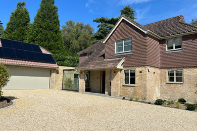 Photo of a large and brown contemporary two floor brick and front house exterior in Surrey with a hip roof, a tiled roof, a brown roof and board and batten cladding.