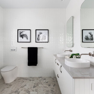 Mid-sized beach style master bathroom in Sydney with recessed-panel cabinets, white cabinets, an open shower, a wall-mount toilet, white tile, porcelain tile, white walls, ceramic floors, a pedestal sink, granite benchtops, beige floor, an open shower, grey benchtops, a double vanity and a floating vanity.