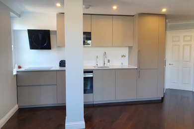 This is an example of a medium sized contemporary single-wall open plan kitchen in London with a single-bowl sink, flat-panel cabinets, beige cabinets, quartz worktops, white splashback, dark hardwood flooring, brown floors and white worktops.