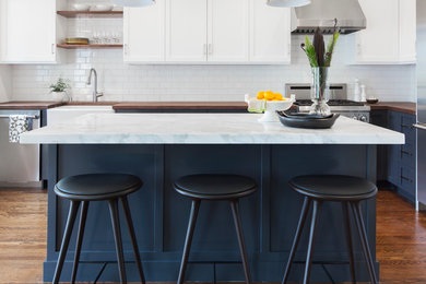 Inspiration for a transitional l-shaped kitchen in San Francisco with a farmhouse sink, shaker cabinets, white cabinets, wood benchtops, white splashback, subway tile splashback, stainless steel appliances, dark hardwood floors and with island.