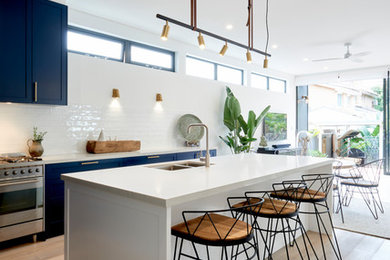 Photo of a contemporary galley eat-in kitchen in Sydney with an undermount sink, shaker cabinets, black cabinets, white splashback, stainless steel appliances, medium hardwood floors, with island, brown floor and white benchtop.