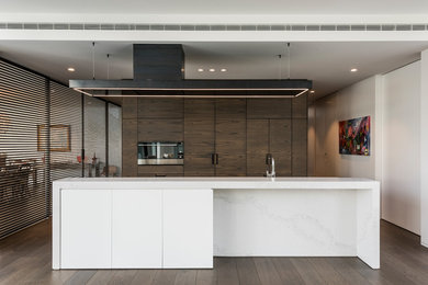 Contemporary galley kitchen pantry in Christchurch with marble benchtops, black appliances, with island and medium wood cabinets.