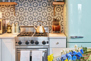Inspiration for a mid-sized eclectic l-shaped medium tone wood floor and brown floor open concept kitchen remodel in New York with a farmhouse sink, shaker cabinets, white cabinets, quartz countertops, multicolored backsplash, cement tile backsplash, stainless steel appliances, an island and gray countertops