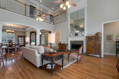 This is an example of a large eclectic open concept living room in New Orleans with grey walls, light hardwood floors, a standard fireplace, a stone fireplace surround and brown floor.