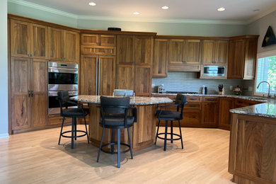 Foto på ett stort vintage beige kök, med en undermonterad diskho, skåp i shakerstil, skåp i mellenmörkt trä, granitbänkskiva, grått stänkskydd, stänkskydd i glaskakel, rostfria vitvaror, ljust trägolv, en köksö och brunt golv