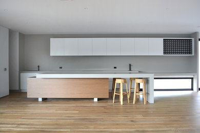 This is an example of a beach style eat-in kitchen in Melbourne with white cabinets, concrete benchtops, stone slab splashback and with island.