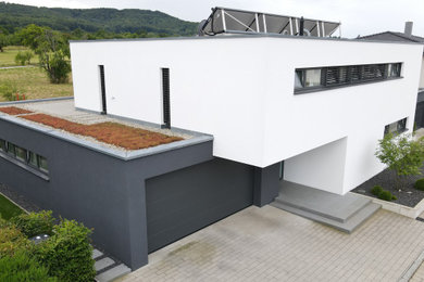 Modelo de fachada de casa blanca moderna de dos plantas con revestimiento de estuco, tejado plano y techo verde