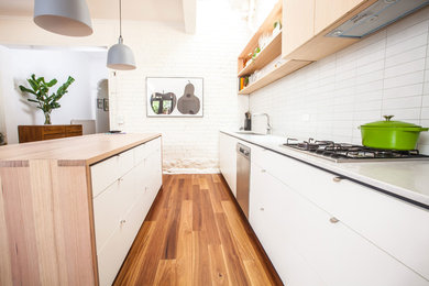 Mid-sized contemporary single-wall eat-in kitchen in Melbourne with a double-bowl sink, flat-panel cabinets, white cabinets, wood benchtops, white splashback, ceramic splashback, stainless steel appliances, medium hardwood floors and with island.