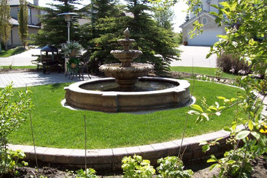 Photo of a mid-sized traditional front yard full sun garden for summer in Calgary with a water feature and concrete pavers.