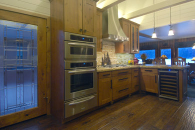 Example of a mid-sized mountain style u-shaped medium tone wood floor eat-in kitchen design in Los Angeles with an undermount sink, shaker cabinets, light wood cabinets, granite countertops, beige backsplash, stone tile backsplash, stainless steel appliances and a peninsula