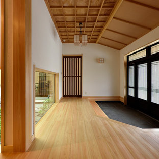 他の地域の大きい引き戸アジアンスタイルのおしゃれな玄関ホール (白い壁、淡色無垢フローリング、黒いドア、茶色い床) の写真