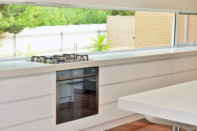 This is an example of a large contemporary galley open plan kitchen in Sydney with an undermount sink, flat-panel cabinets, white cabinets, quartz benchtops, stainless steel appliances, medium hardwood floors and with island.