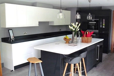 Photo of a large modern galley open plan kitchen in Kent with a double-bowl sink, flat-panel cabinets, quartz worktops, black appliances, an island and grey floors.