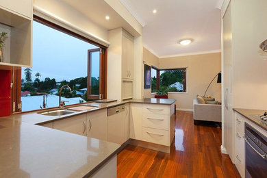 Inspiration for a mid-sized contemporary u-shaped open plan kitchen in Brisbane with an undermount sink, flat-panel cabinets, white cabinets, quartz benchtops, red splashback, glass sheet splashback, stainless steel appliances, medium hardwood floors, no island and beige benchtop.