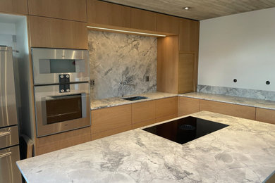 Bild på ett stort nordiskt grå grått kök, med en enkel diskho, släta luckor, skåp i ljust trä, bänkskiva i kvartsit, grått stänkskydd, rostfria vitvaror, klinkergolv i keramik, en köksö och grått golv