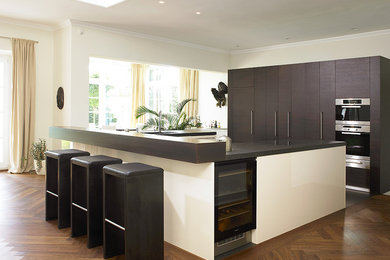 This is an example of a contemporary u-shaped open plan kitchen in Other with flat-panel cabinets, brown cabinets, black appliances and medium hardwood floors.