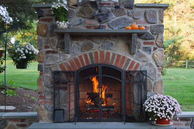 This is an example of a mid-sized country backyard patio in Philadelphia with with fireplace, brick pavers and no cover.