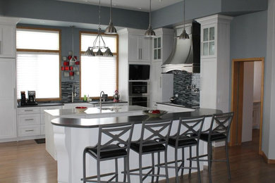 Inspiration for a mid-sized transitional u-shaped medium tone wood floor and brown floor open concept kitchen remodel in Calgary with a farmhouse sink, shaker cabinets, white cabinets, solid surface countertops, gray backsplash, matchstick tile backsplash, stainless steel appliances and an island