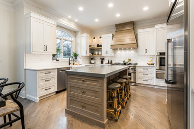 Example of a large country u-shaped medium tone wood floor and brown floor open concept kitchen design in Chicago with a farmhouse sink, shaker cabinets, white cabinets, quartz countertops, white backsplash, ceramic backsplash, stainless steel appliances, an island and white countertops