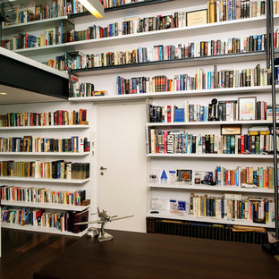 This is an example of a modern home office and library in Tel Aviv with white walls and dark hardwood flooring.