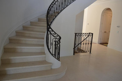 Diseño de escalera curva clásica grande con escalones de piedra caliza, contrahuellas de piedra caliza y barandilla de metal
