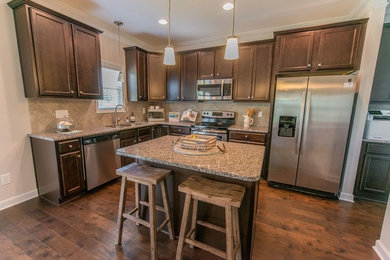 Mid-sized transitional l-shaped eat-in kitchen in Raleigh with a double-bowl sink, recessed-panel cabinets, dark wood cabinets, granite benchtops, beige splashback, porcelain splashback, stainless steel appliances, medium hardwood floors, with island, brown floor and multi-coloured benchtop.