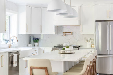 Inspiration for a large country l-shaped kitchen/diner in Vancouver with a belfast sink, shaker cabinets, white cabinets, engineered stone countertops, white splashback, engineered quartz splashback, stainless steel appliances, medium hardwood flooring, an island, beige floors and white worktops.