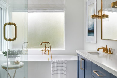 This is an example of a transitional master bathroom in Toronto with shaker cabinets, blue cabinets, a freestanding tub, an alcove shower, gray tile, white tile, white walls, an undermount sink, engineered quartz benchtops, multi-coloured floor, a hinged shower door, white benchtops, a single vanity and a built-in vanity.