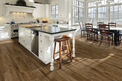 Mid-sized transitional l-shaped medium tone wood floor eat-in kitchen photo in Denver with a farmhouse sink, shaker cabinets, white cabinets, granite countertops, white backsplash, ceramic backsplash, stainless steel appliances and an island