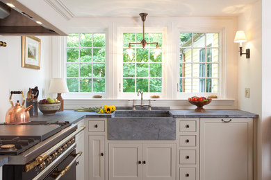 Inspiration for a mid-sized country l-shaped eat-in kitchen in Boston with soapstone benchtops, black appliances, recessed-panel cabinets, a farmhouse sink, green cabinets, beige splashback, ceramic splashback, medium hardwood floors, no island and brown floor.
