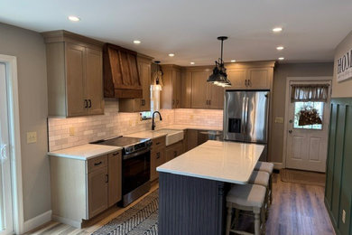 Example of a mid-sized transitional l-shaped vinyl floor and brown floor eat-in kitchen design in Manchester with a farmhouse sink, shaker cabinets, light wood cabinets, quartz countertops, beige backsplash, subway tile backsplash, stainless steel appliances, an island and beige countertops