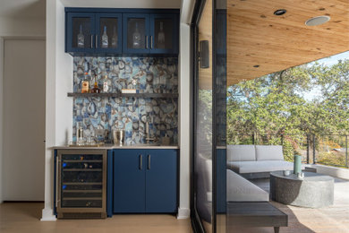 Wet bar - small contemporary single-wall light wood floor wet bar idea in Austin with an undermount sink, glass-front cabinets, blue cabinets, quartz countertops, blue backsplash, glass tile backsplash and gray countertops