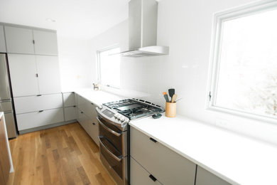 Eat-in kitchen - mid-century modern l-shaped medium tone wood floor and brown floor eat-in kitchen idea in Charlotte with an undermount sink, flat-panel cabinets, gray cabinets, quartz countertops, white backsplash, stainless steel appliances and an island