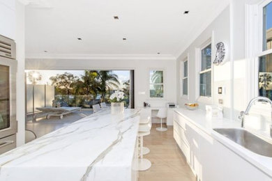 This is an example of a large modern galley eat-in kitchen in Sydney with a drop-in sink, marble benchtops, white splashback, glass sheet splashback, stainless steel appliances, light hardwood floors, with island and grey floor.
