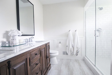 Inspiration for a mid-sized country master white tile and subway tile vinyl floor and gray floor double shower remodel in Minneapolis with brown cabinets, a two-piece toilet, white walls, an undermount sink, marble countertops, a hinged shower door and white countertops