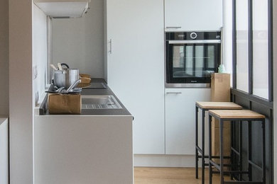 Foto de cocinas en L moderna pequeña con fregadero bajoencimera, puertas de armario blancas, encimera de laminado y suelo de madera clara