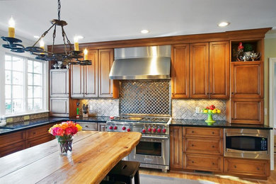 Inspiration for a mid-sized rustic l-shaped medium tone wood floor and brown floor open concept kitchen remodel in Orange County with an undermount sink, raised-panel cabinets, medium tone wood cabinets, granite countertops, beige backsplash, ceramic backsplash, stainless steel appliances and an island