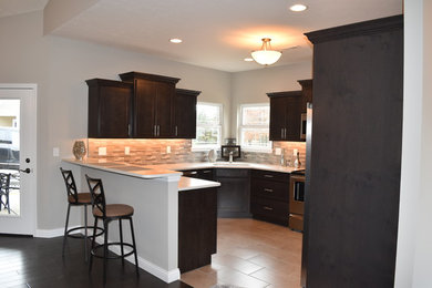 Enclosed kitchen - mid-sized traditional l-shaped travertine floor enclosed kitchen idea in Other with an undermount sink, shaker cabinets, dark wood cabinets, quartz countertops, gray backsplash, glass tile backsplash, stainless steel appliances and a peninsula