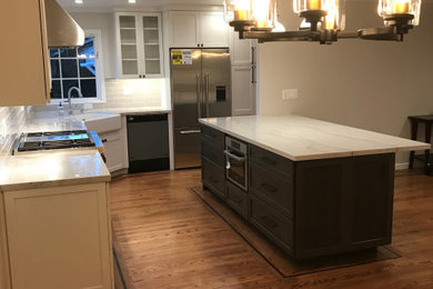 Eat-in kitchen - mid-sized traditional l-shaped medium tone wood floor and brown floor eat-in kitchen idea in San Francisco with a farmhouse sink, shaker cabinets, white cabinets, quartz countertops, white backsplash, porcelain backsplash, stainless steel appliances, an island and white countertops