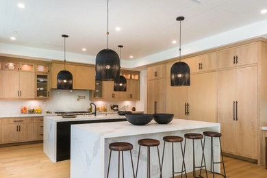 Inspiration for a contemporary eat-in kitchen in Los Angeles with an undermount sink, flat-panel cabinets, light wood cabinets, quartz benchtops, white splashback, stone slab splashback, stainless steel appliances, light hardwood floors, multiple islands, beige floor and white benchtop.