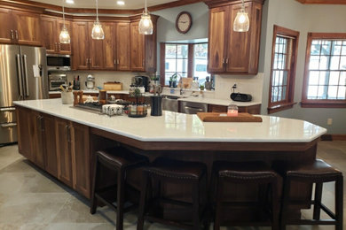 Eat-in kitchen - traditional l-shaped porcelain tile and beige floor eat-in kitchen idea in Other with a farmhouse sink, flat-panel cabinets, brown cabinets, quartz countertops, white backsplash, porcelain backsplash, stainless steel appliances, an island and white countertops