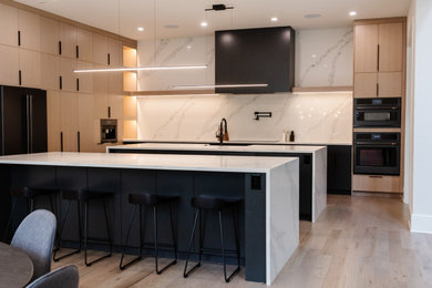 This is an example of a kitchen in Atlanta with a belfast sink, flat-panel cabinets, light wood cabinets, white splashback, light hardwood flooring, multiple islands and white worktops.