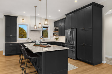 Example of a large transitional l-shaped light wood floor and brown floor eat-in kitchen design with a farmhouse sink, flat-panel cabinets, gray cabinets, quartz countertops, white backsplash, ceramic backsplash, stainless steel appliances, an island and white countertops