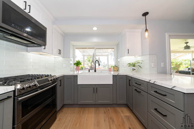 Eat-in kitchen - mid-sized contemporary u-shaped medium tone wood floor and brown floor eat-in kitchen idea in Los Angeles with a farmhouse sink, shaker cabinets, white cabinets, quartz countertops, white backsplash, subway tile backsplash, stainless steel appliances, a peninsula and white countertops