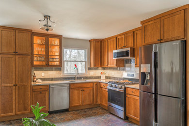 Mid-sized transitional l-shaped eat-in kitchen photo in New York with an undermount sink, shaker cabinets, medium tone wood cabinets, granite countertops, beige backsplash, ceramic backsplash, stainless steel appliances, no island and beige countertops
