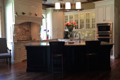 Example of a classic dark wood floor kitchen design in Orlando with a farmhouse sink, raised-panel cabinets, granite countertops, multicolored backsplash, stone slab backsplash, stainless steel appliances and an island
