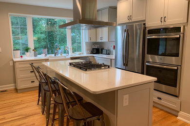 Inspiration for a mid-sized transitional l-shaped medium tone wood floor eat-in kitchen remodel in Baltimore with a farmhouse sink, shaker cabinets, gray cabinets, quartz countertops, white backsplash, subway tile backsplash, stainless steel appliances, an island and white countertops